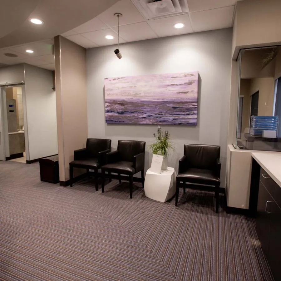 Modern waiting room with black chairs, abstract wall art, and a white side table with a plant.
