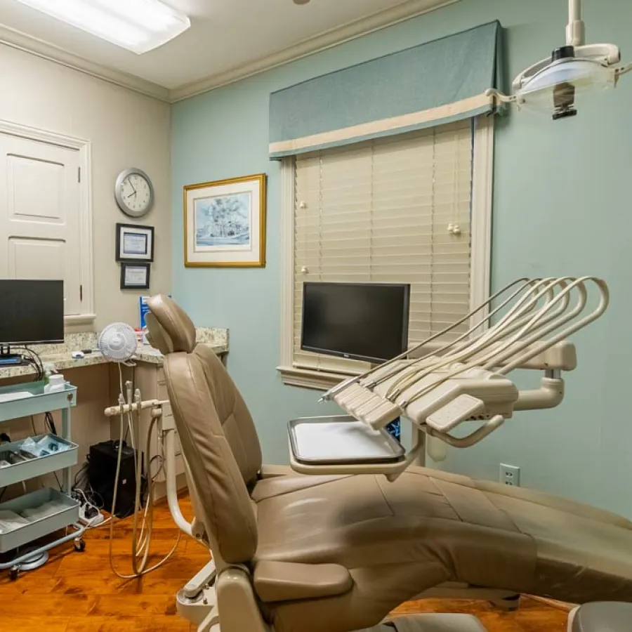 Modern dental office with beige patient chair, dental equipment, computer monitors, and light blue walls.