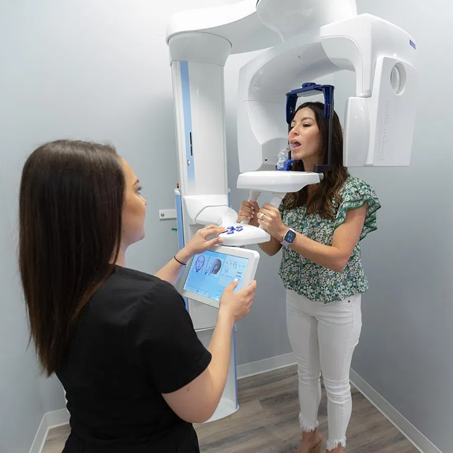 Woman undergoing a dental 3D X-ray scan with a technician operating the machine in a clinical room.