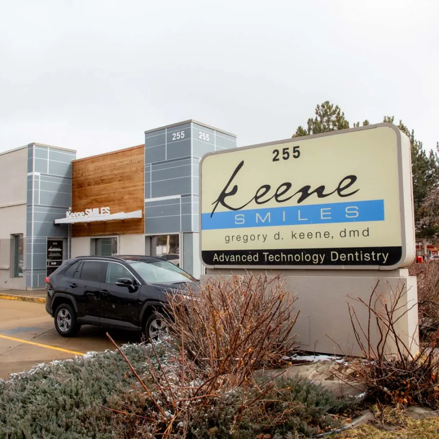 Exterior view of Keene Smiles dental office with signage and parked black SUV on a cloudy day.
