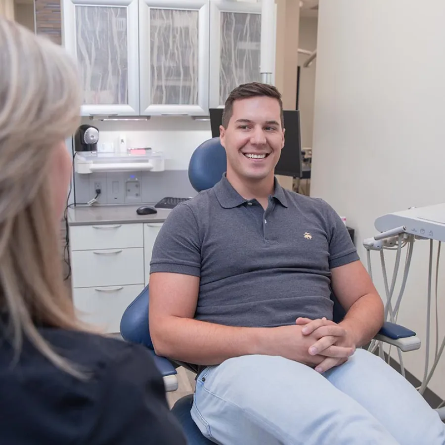 Smiling man sitting in a dental chair talking to a female dentist in a modern clinic room.