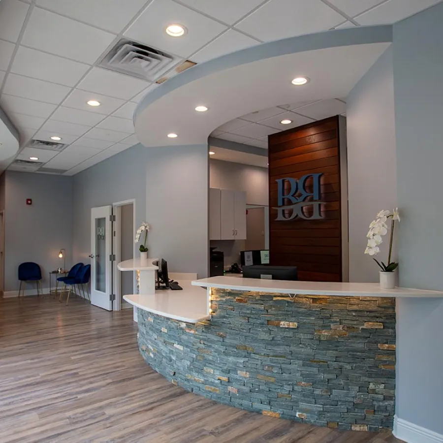 Modern medical office reception area with stone counter, wooden panel backdrop, and blue seating in waiting area.