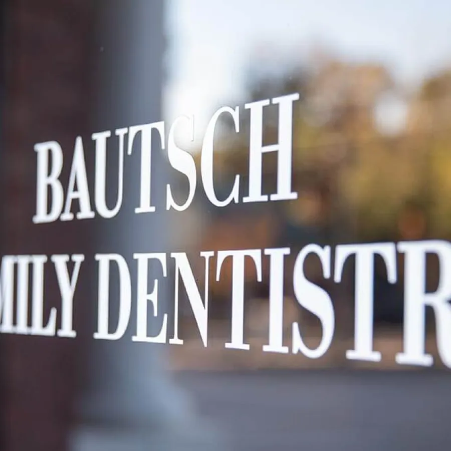 Close-up of Bautsch Family Dentistry sign on glass door with blurred outdoor background.