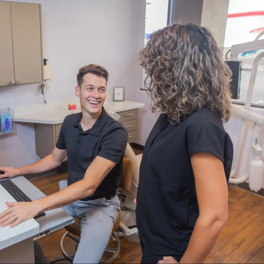 Dental office staff smiling and interacting at the reception desk with computer and dental equipment.