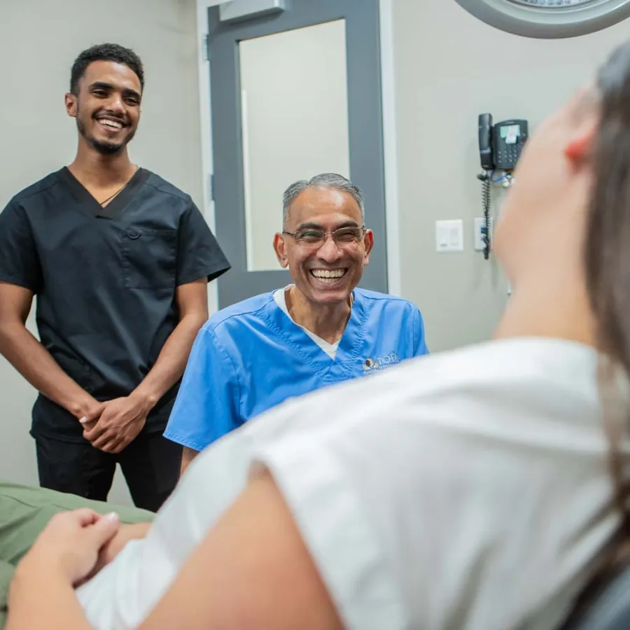Smiling dentist and assistant talking to a female patient in a dental office, creating a friendly atmosphere