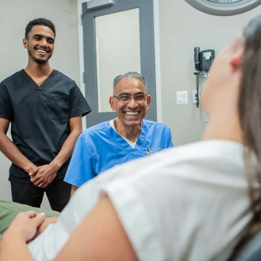 Smiling dentist and assistant talking to a female patient in a dental office, creating a friendly atmosphere