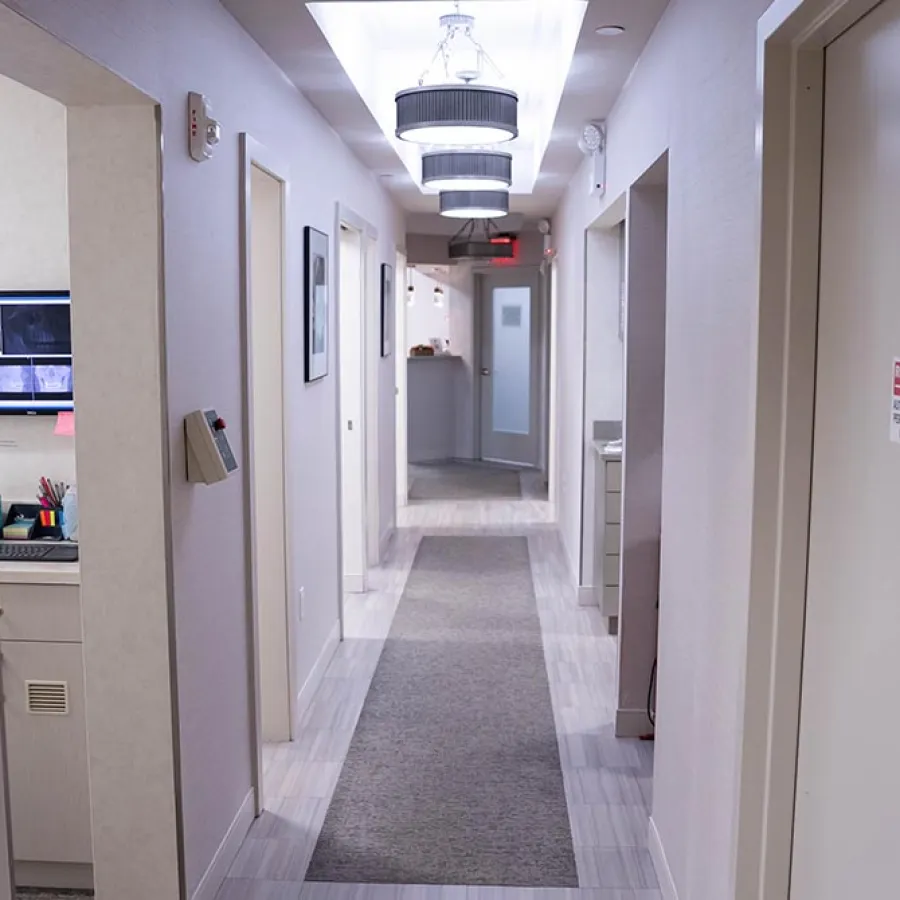 Clean, modern hallway in a medical or office building with gray carpet runner and ceiling lights.