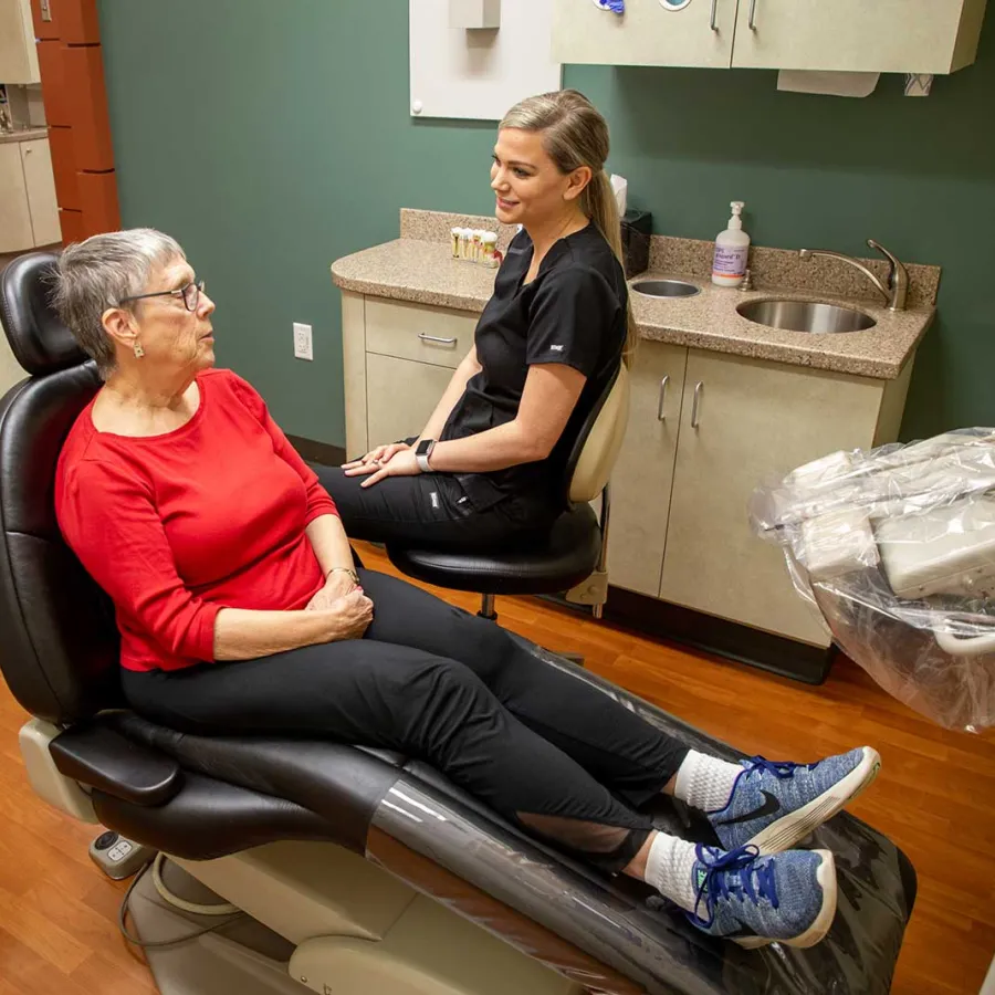 Elderly woman in red shirt consulting with female dentist in modern dental office room.