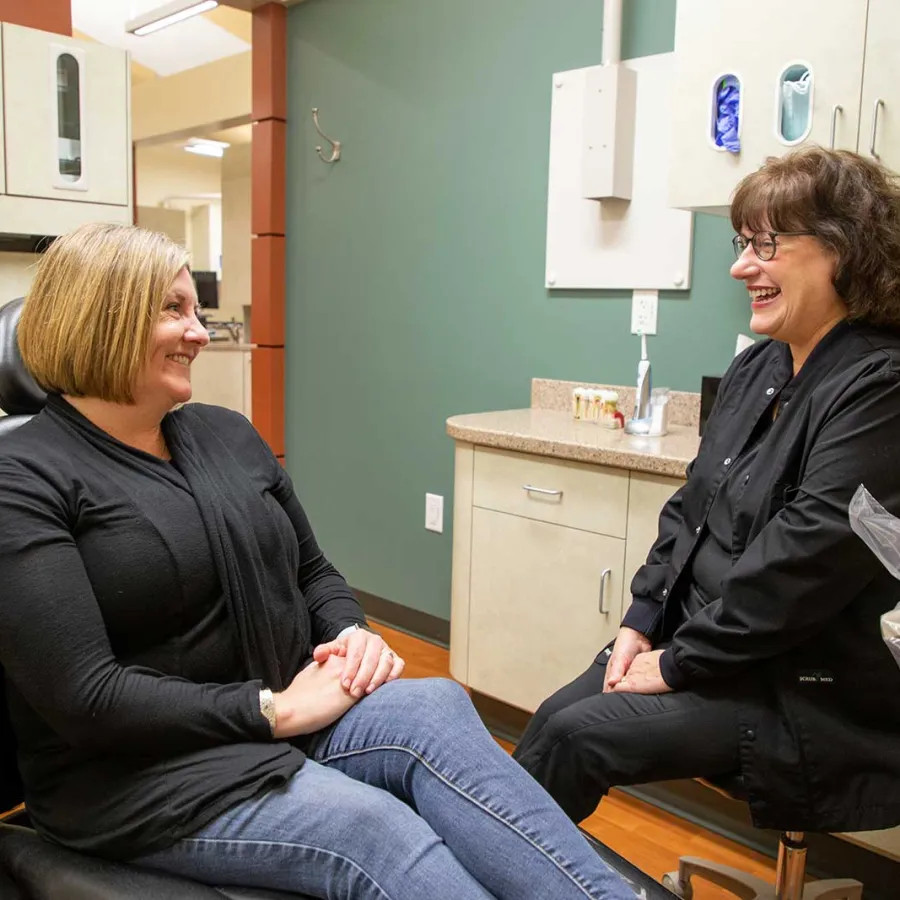 Patient and dental professional smiling and conversing in a modern dental office consultation room.