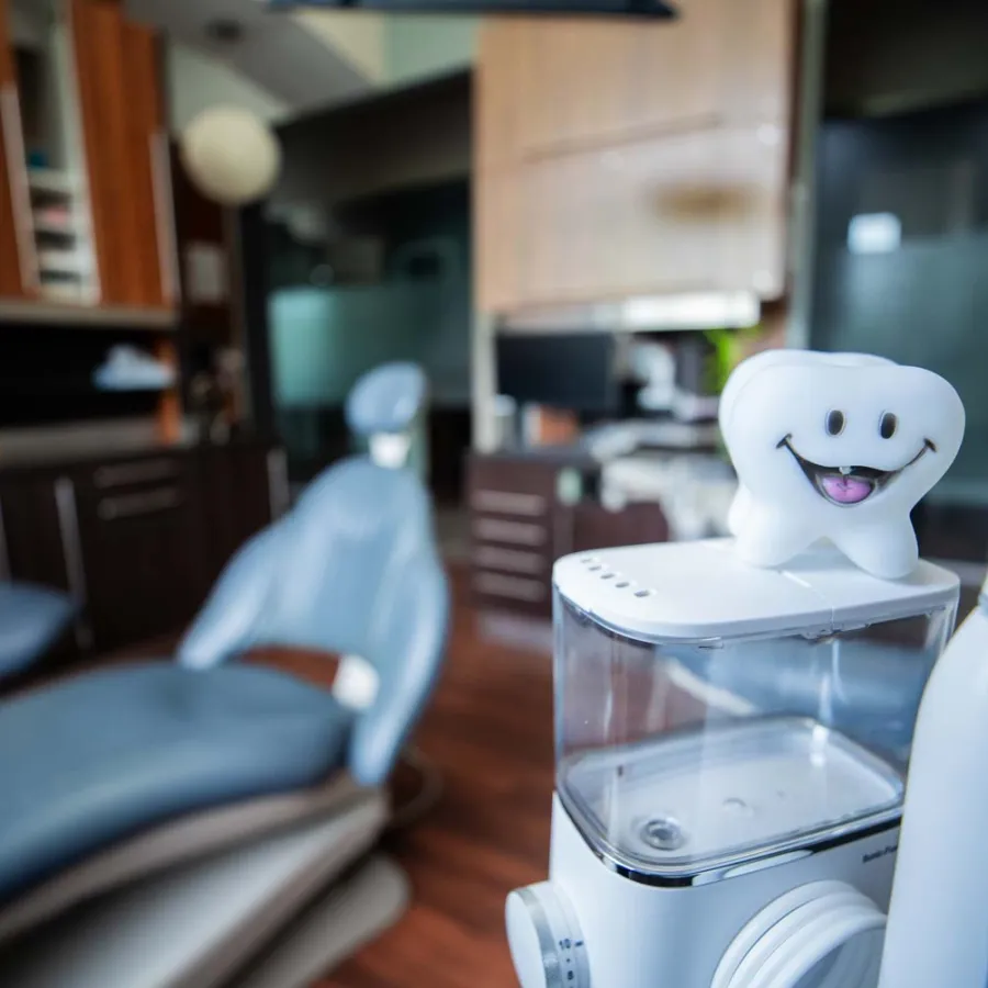 Smiling tooth figurine and electric toothbrush in a modern dental clinic with chair and wooden cabinets.