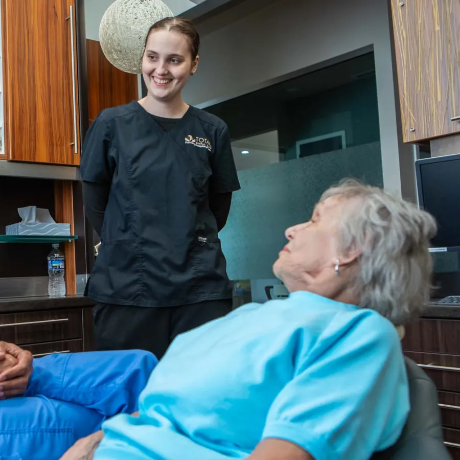 Dentist consulting elderly female patient in dental office with assistant smiling in background