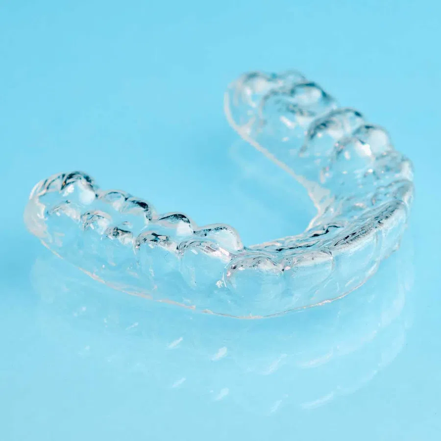 Transparent dental aligner on a blue reflective surface used for teeth straightening.