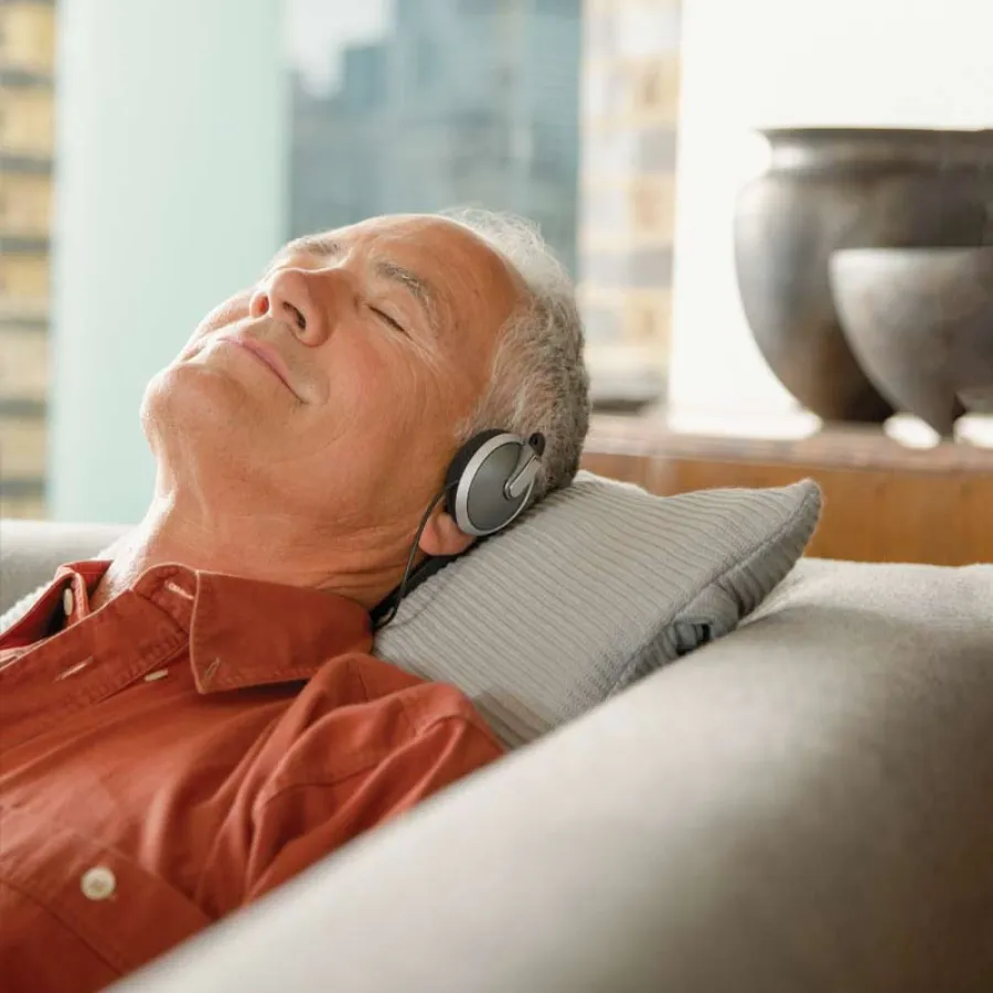 Older man relaxing on a couch with headphones on, eyes closed, enjoying music or meditation.