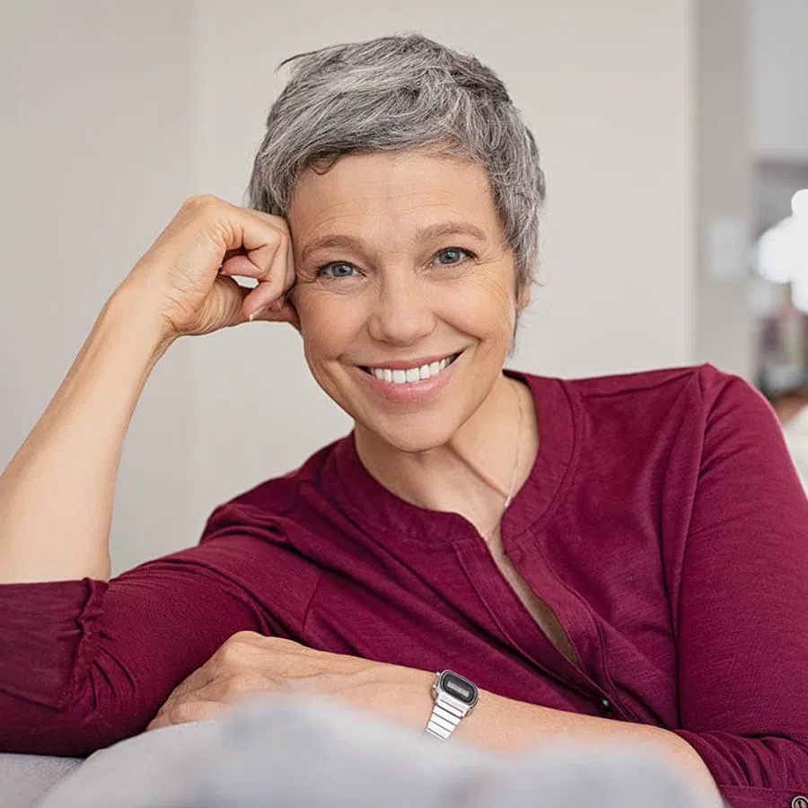Smiling woman with gray hair in a maroon shirt, sitting comfortably and resting her chin on her hand.
