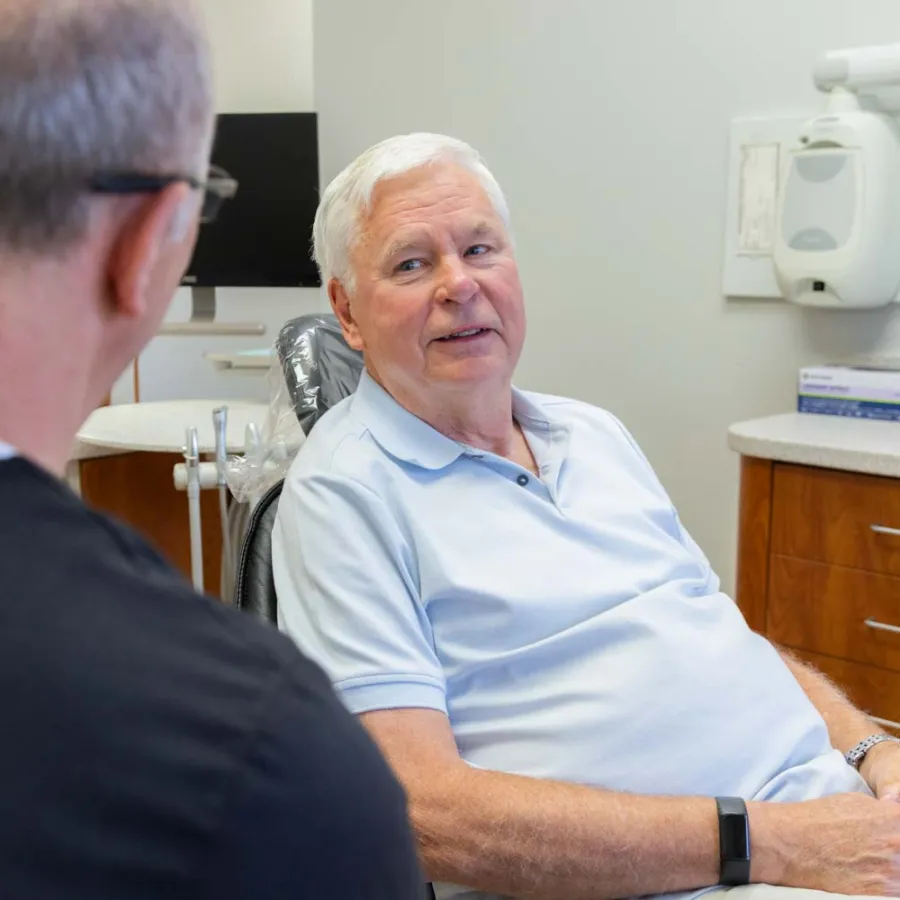 Senior man in light blue shirt consulting with dentist in a modern dental office setting.