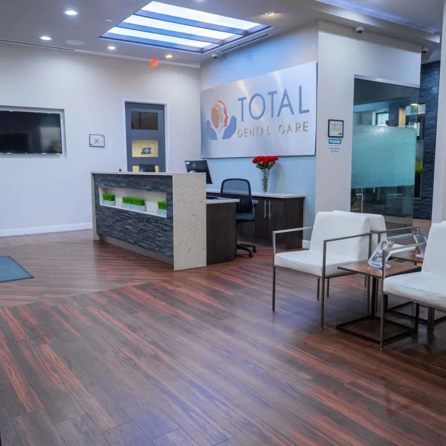 Modern dental office reception area with wooden floors, white chairs, and Total Dental Care sign on wall