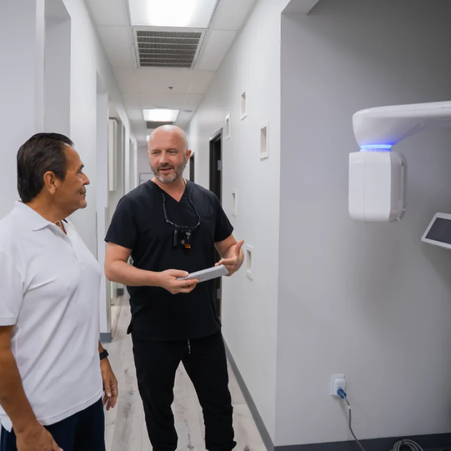 Dentist in black scrubs discussing treatment with a patient in a modern dental clinic hallway