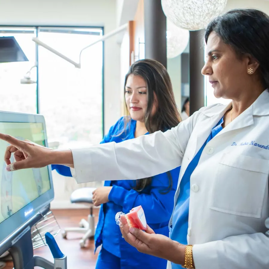Female dentist pointing at dental X-ray on screen while holding a teeth model in a modern dental clinic.
