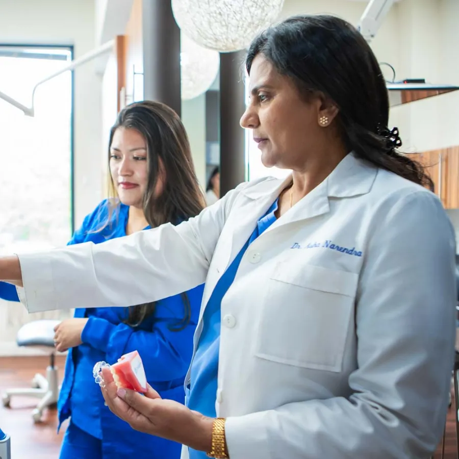 Female dentist pointing at dental X-ray on screen while holding a teeth model in a modern dental clinic.