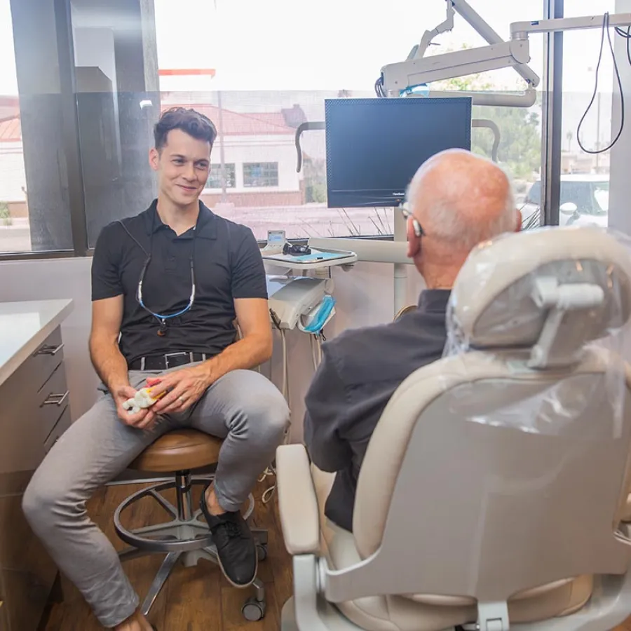 Dentist smiling and talking with a senior patient in a bright dental office with equipment.