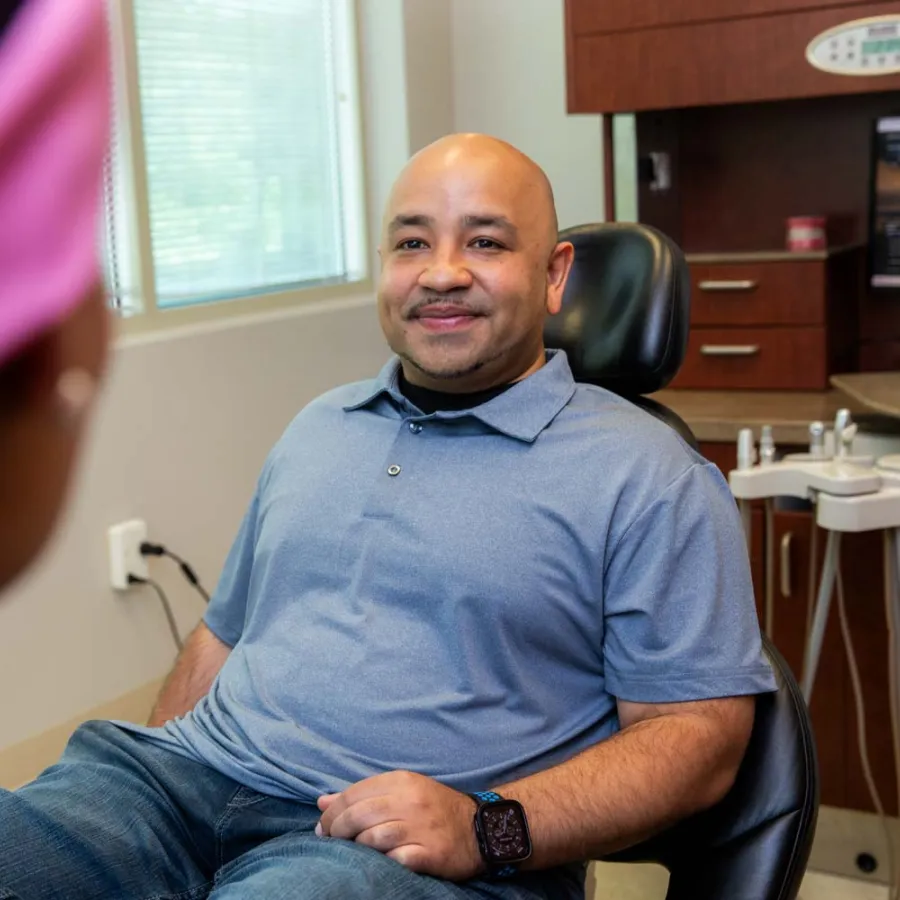 Smiling man sitting in a dental chair talking to a female dentist in a modern dental office.