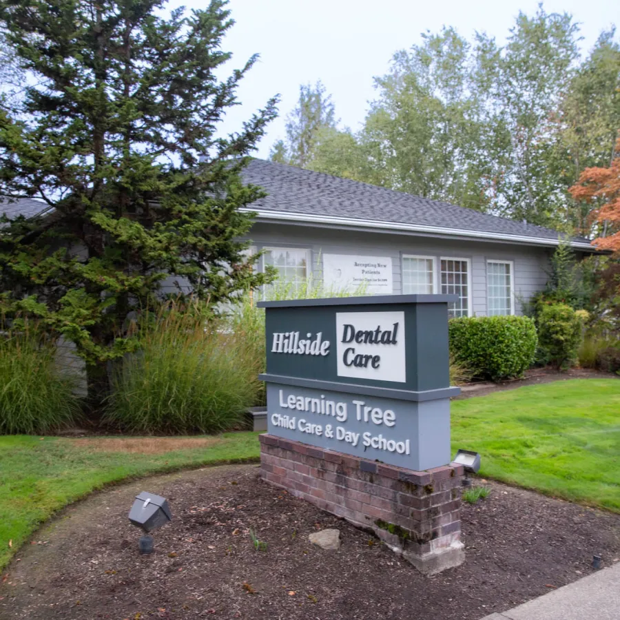 Building with sign displaying Hillside Dental Care and Learning Tree Child Care & Day School surrounded by greenery