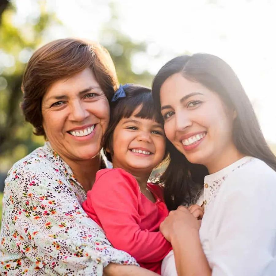 Three generations of women smiling outdoors, embracing and enjoying a sunny day together.