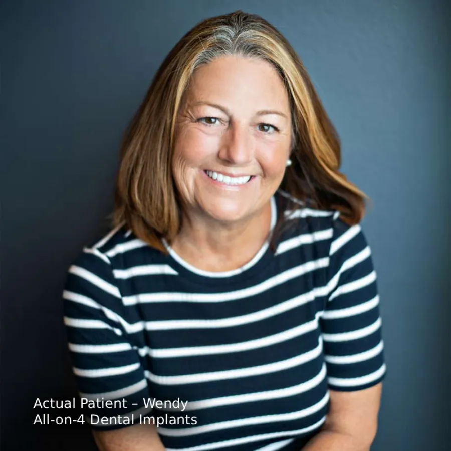 Smiling middle-aged woman with blonde hair wearing a black and white striped shirt against a dark background.
