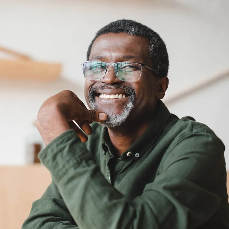 A smiling older man in glasses poses confidently, wearing a green shirt and sitting indoors.