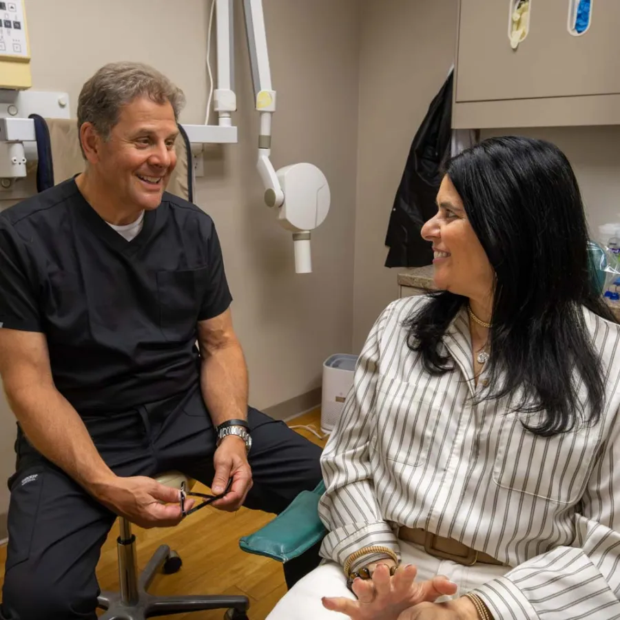 Smiling doctor and patient engage in conversation in a medical office with clinical equipment in the background