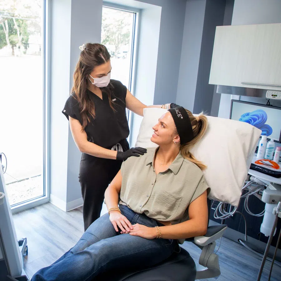 Woman receiving skincare consultation from masked professional in modern clinic with advanced equipment.