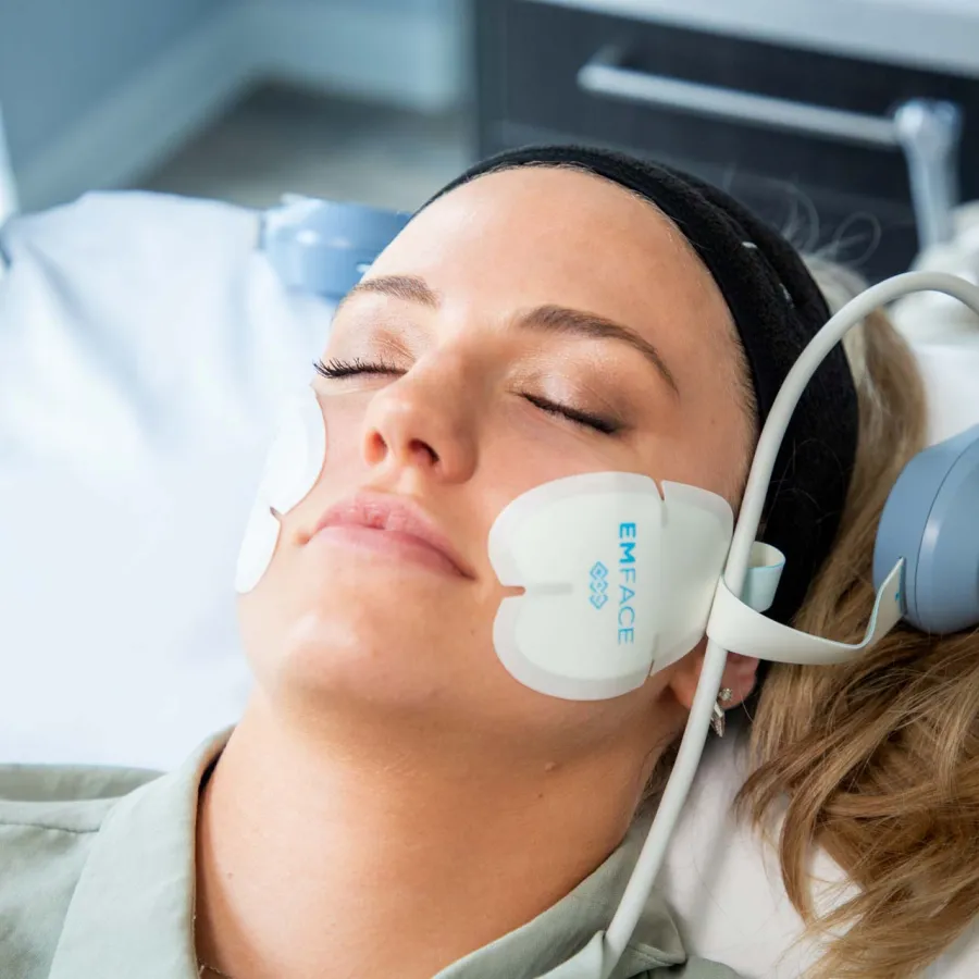 Woman resting with EMFACE facial treatment pads on cheeks undergoing skin therapy
