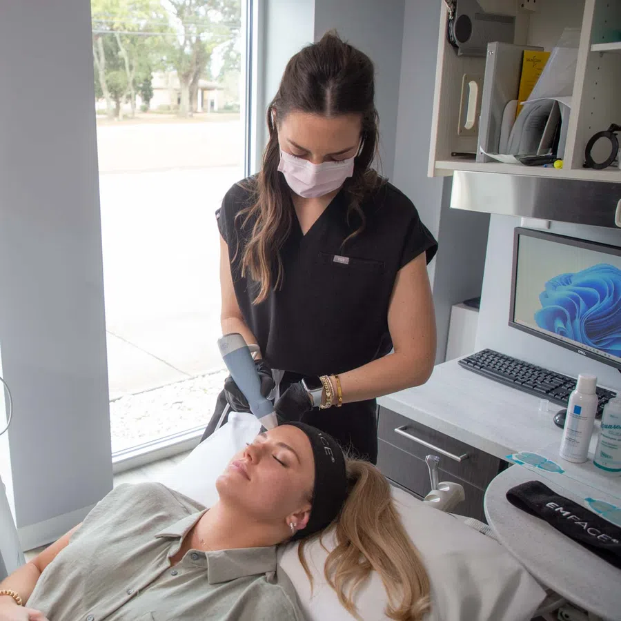 A woman receiving a facial treatment from a skincare professional wearing a mask in a modern clinic room.
