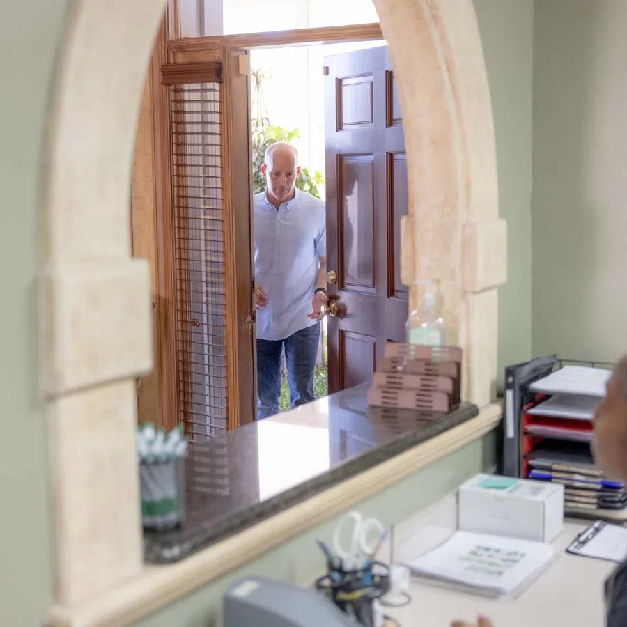 Woman sitting at desk looking at man opening the door in a home office with mirror reflection.