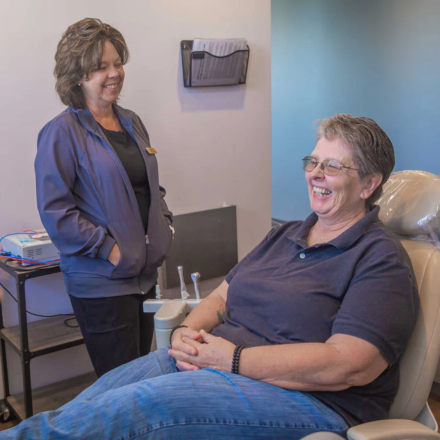 Dental hygienist reviewing patient information with smiling woman in bright orange top in modern dental office