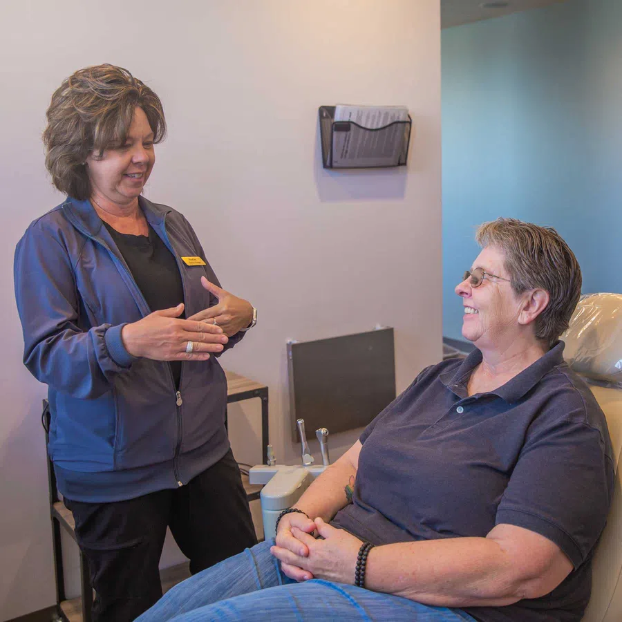 Dental hygienist talks to smiling patient sitting in a dental chair in a clean clinic room.