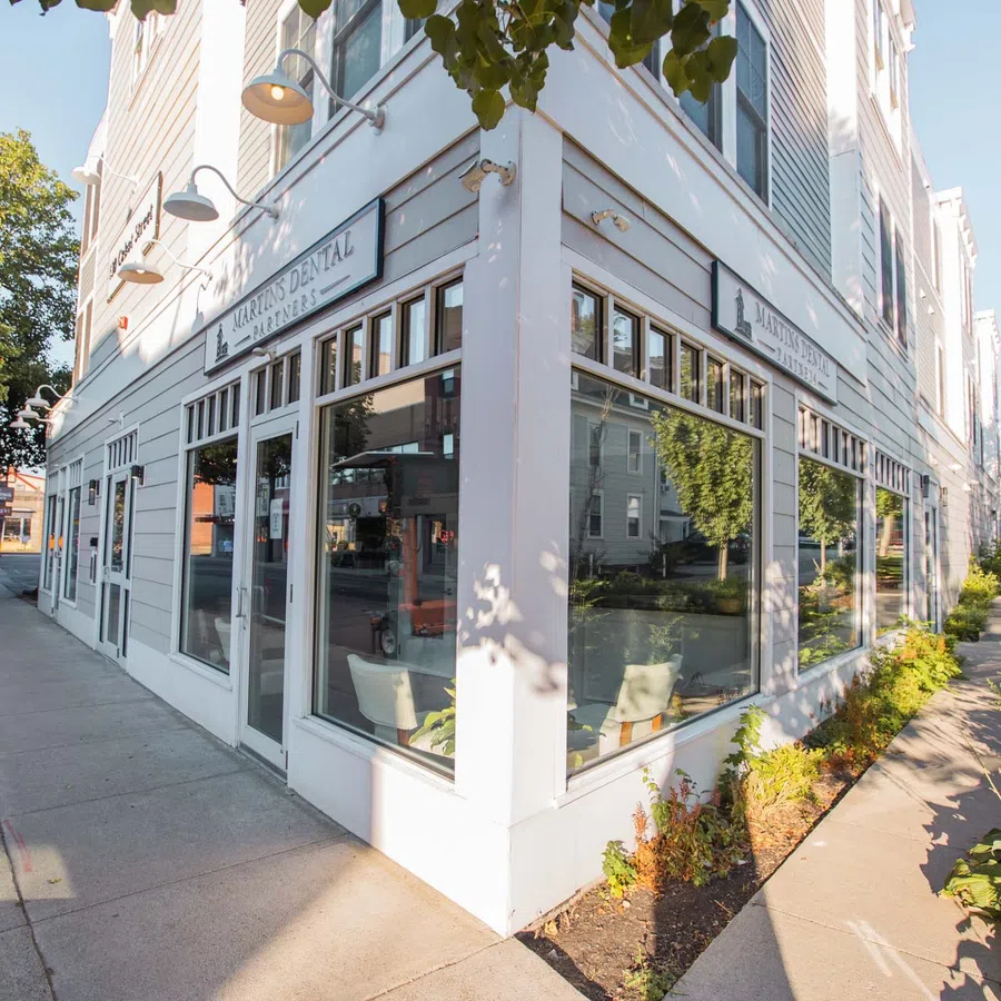 Corner view of a white dental office building with large windows and surrounding sidewalks and greenery.