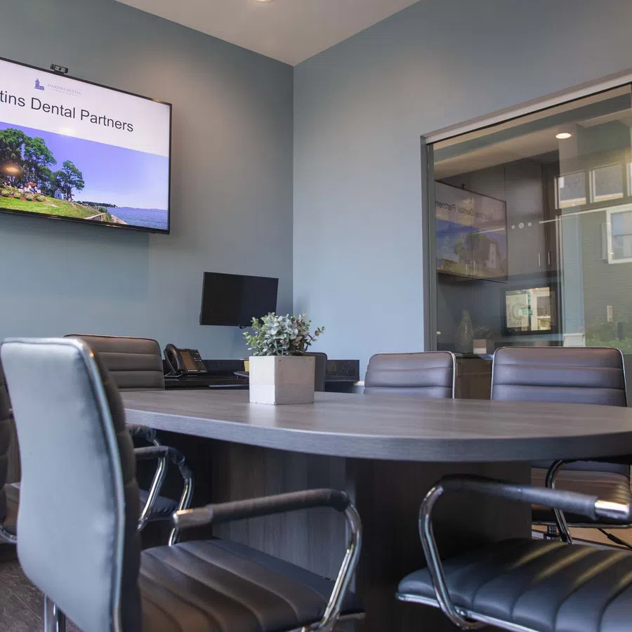Modern conference room with round table, black leather chairs, and a screen displaying Martins Dental Partners.
