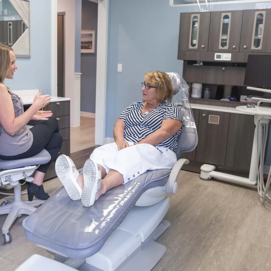 Woman in striped shirt sitting in dental chair talking to dental hygienist in modern clinic