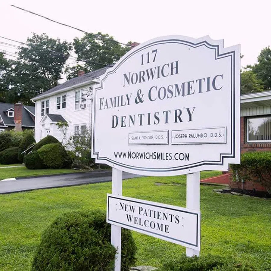 Sign outside Norwich Family & Cosmetic Dentistry office welcoming new patients on a green lawn.