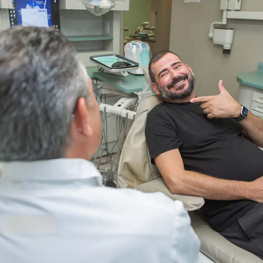 Smiling man pointing to his teeth while sitting in a dental chair during a dentist consultation session.