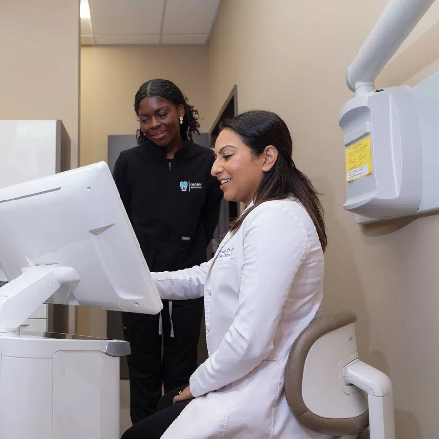 Dentist and dental assistant reviewing patient information on a computer in a modern dental office.