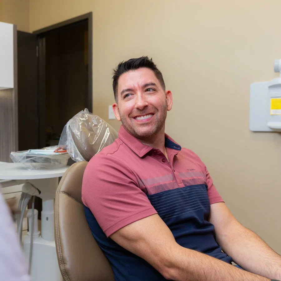 Man smiling while sitting in a dental chair talking to a dentist in a bright dental office.
