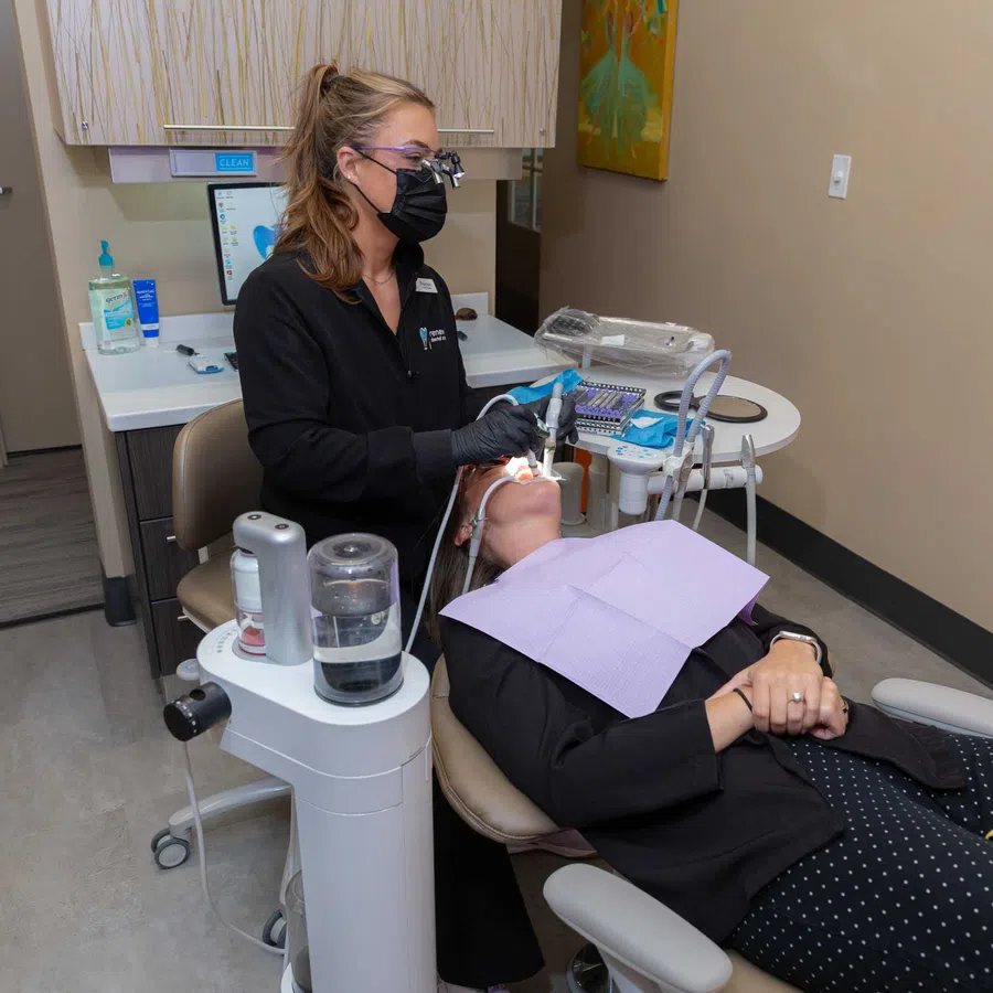 Dentist wearing black mask treats patient lying back in dental chair during oral procedure in clinic.