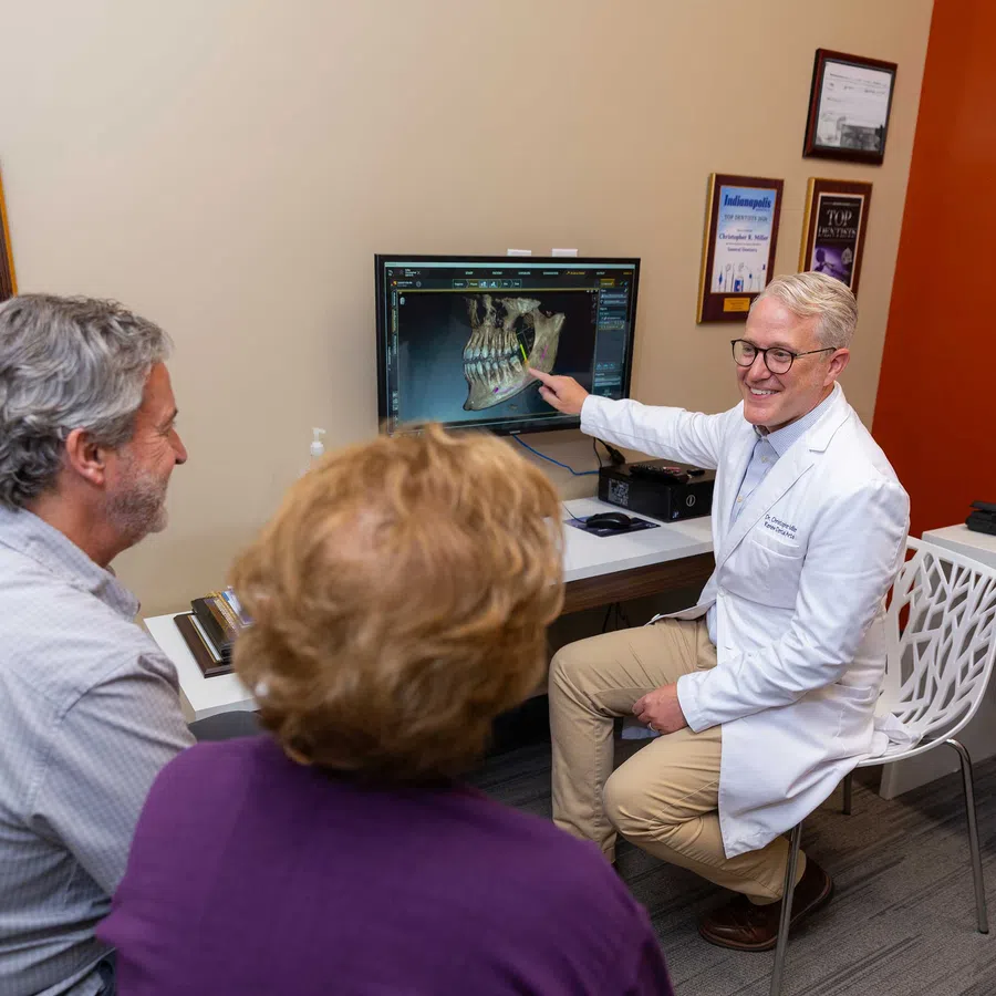 Dentist explaining dental X-ray results to a middle-aged couple in a modern consultation room.