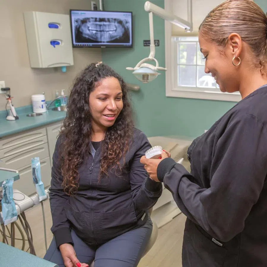 Dentist showing dental mold to patient in clinic with dental X-ray on monitor
