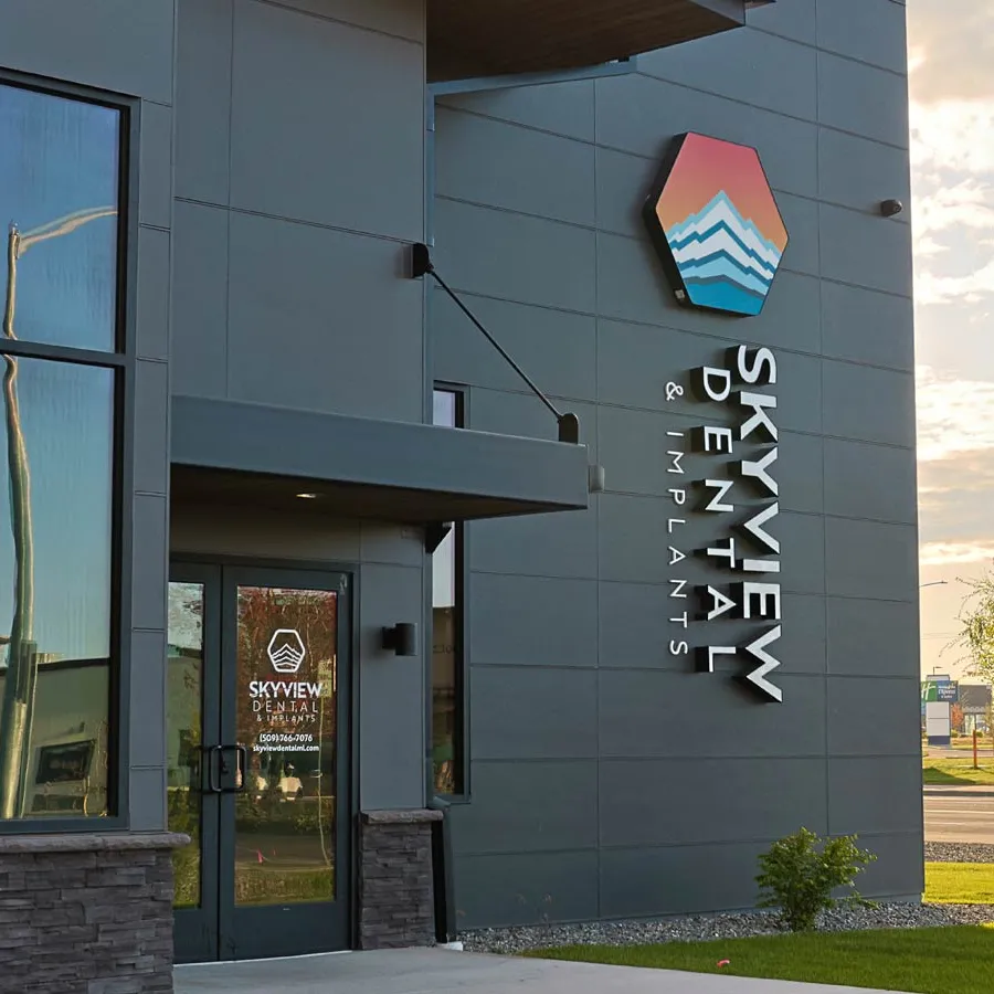 Exterior view of Skyview Dental & Implants building with signage and a glass door at sunset.