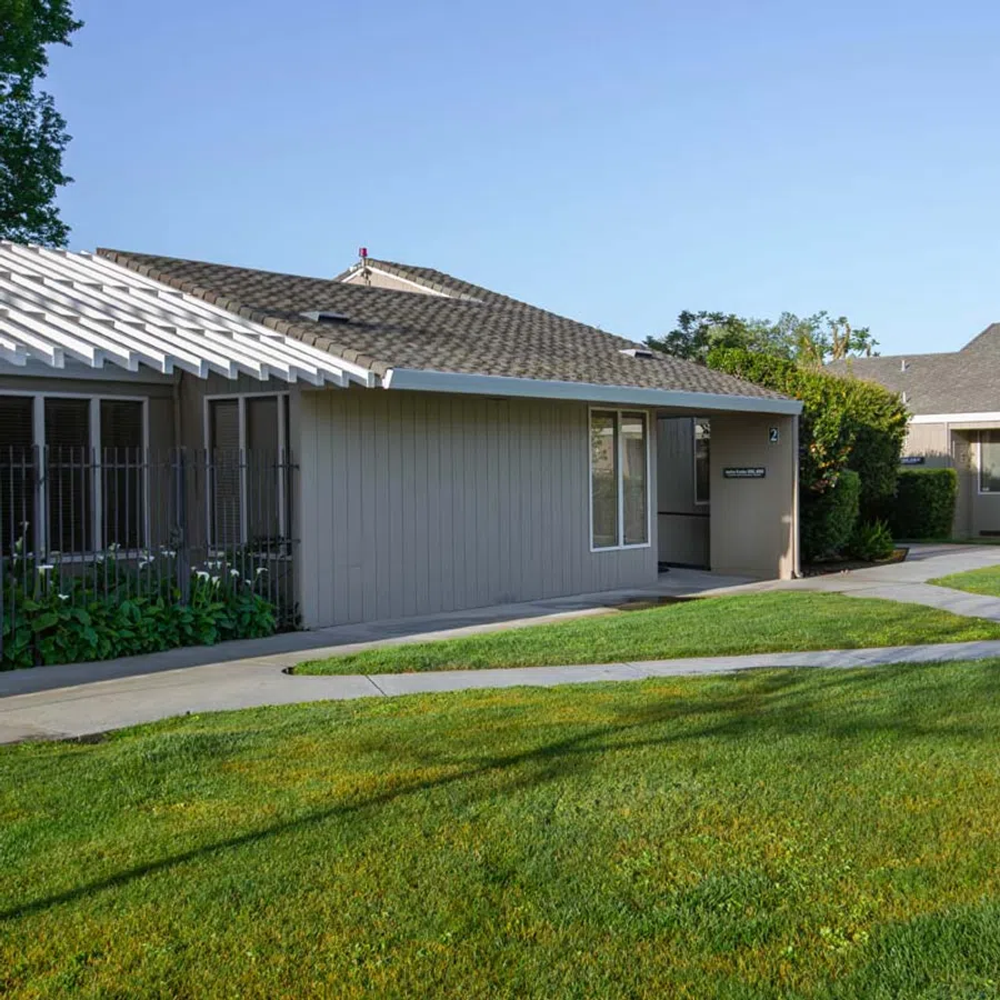 Single-story residential building with beige siding, large windows, and a well-maintained green lawn under a clear sky.