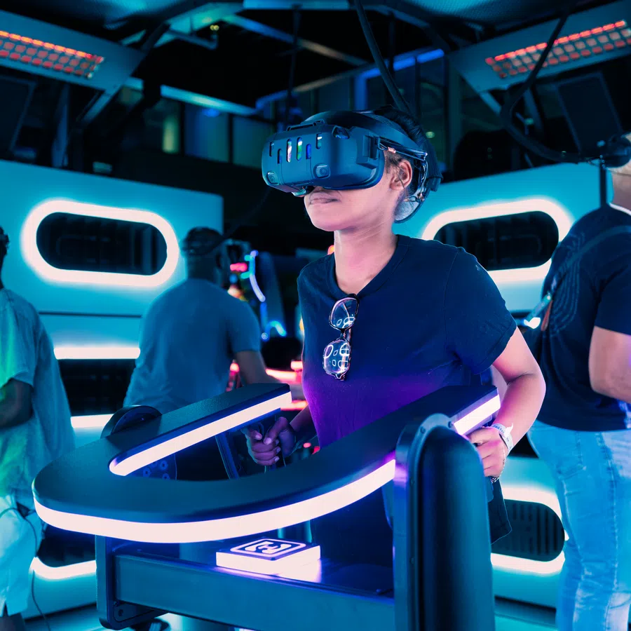 People experiencing virtual reality games using VR headsets and interactive motion controllers in a neon-lit arcade.