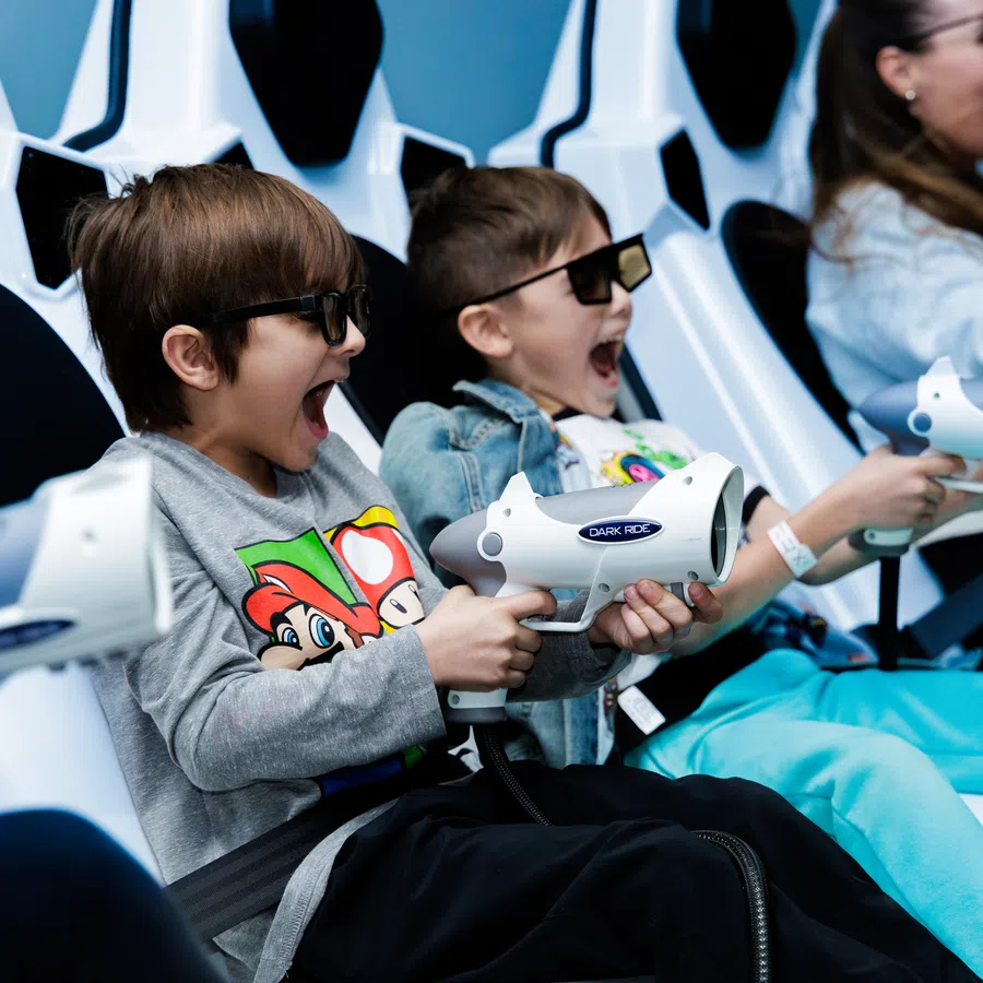 Children wearing 3D glasses and holding toy guns enjoy an interactive arcade shooting game.